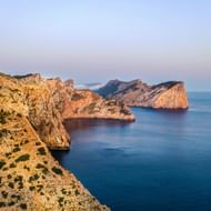 Dramatische kalkstenen kliffen aan de linkerkant met uitzicht op de kalme donkerblauwe Middellandse Zee op Mallorca. Mistige blauwe lucht op de achtergrond.