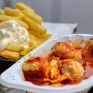 Witte bak met gesneden currywurst in rode currysaus, geserveerd met gouden frietjes met witte mayonaise erbovenop.