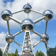 Het Atomium in Brussel, een grote metalen structuur met 9 onderling verbonden bollen die atomen voorstellen, tegen een blauwe hemel met wolken.