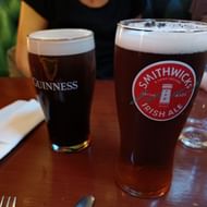 Ierse bieren op de Dingle Way wandelroute Twee pinten Iers bier op houten tafel - Guinness met donkere stout en romig schuim, en Smithwick's Irish Ale met amberkleur en wit schuim.