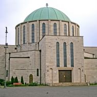 Moderne Votiekerk in Mohács met kenmerkende groene koperen koepel en kruis bovenop. Het beige stenen gebouw heeft hoge boogvensters.