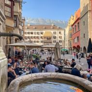 Stenen fontein in Innsbrucks oude stad met buitenterras. Kleurrijke historische gebouwen en besneeuwde bergen op de achtergrond.