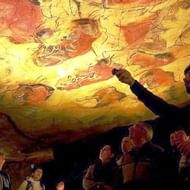 Reisgids wijst naar prehistorische grotschilderingen op geel-oranje rotsplafond terwijl groep bezoekers opkijkt in Spaanse grot.
