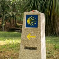 Stenen wegmarkering op Portugese Camino met gele schelp op blauwe achtergrond, gele pijl en afstandsaanduiding Km 83,250.