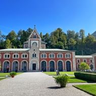 Rood-wit gebouw van Alte Saline in Bad Reichenhall met kapeltoren, boogfaçade, verzorgd gazon en grindpad onder blauwe lucht.