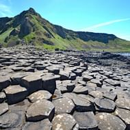 Giant's Causeway met duizenden zeshoekige basaltzuilen die zich uitstrekken naar de zee met groene heuvels en blauwe lucht in Noord-Ierland.