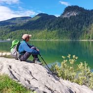 Wandelaar bij Schwarzensee meer Vrouwelijke wandelaar met groene rugzak en wandelstokken zit op rotsachtige oever van Schwarzensee meer, omringd door beboste bergen.
