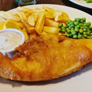 Goudgele vis in beslag met dikke friet, erwtensoep en tartaarsaus op een wit bord. Klassieke Britse pub maaltijd.