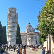 De beroemde Scheve Toren van Pisa staat prominent naast de kathedraal van Pisa onder een heldere blauwe hemel, met toeristen op het plein.