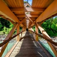 Overdekte houten fietsbrug in Feldkirch, Oostenrijk, met houtskeletbouw over turquoise rivierwater omgeven door groene bomen.