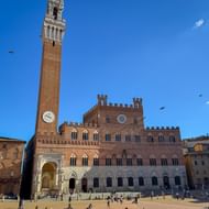 Piazza del Campo in Siena met het middeleeuwse Palazzo Pubblico en zijn hoge Torre del Mangia toren tegen een blauwe lucht. Bezoekers op het plein.