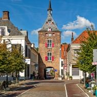 Historische bakstenen poort met klok en rode luiken staat in het centrum van Vianens marktplein, omringd door traditionele huizen.
