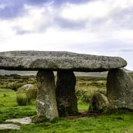 Neolithische dolmen in Cornwall met grote platte dekplaat op drie rechtopstaande stenen in groen heidelandschap onder bewolkte hemel.