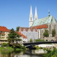 Gotische kathedraal met tweelingtorens en groen koperen dak in Görlitz, gezien vanaf rivieroever met brug en historische gebouwen.