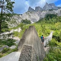 Hangbrug in Klausbach vallei, Nationaal Park Berchtesgaden, met wandelaars en dramatische Alpentoppen op de achtergrond.