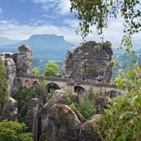 De beroemde Bastei-brug die zich uitstrekt tussen torenhoge zandstenen rotsformaties in Saksisch Zwitserland, omgeven door weelderig groen bos.