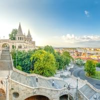 Panoramisch uitzicht vanaf de Vissersbastion in Boedapest met neogotische torens, stenen terrassen en de Donau met stadshorizon erachter.