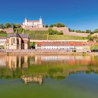 Festung Marienberg fort op een heuvel met wijngaarden in Würzburg, weerspiegeld in de Main. Kleurrijke gebouwen langs de waterkant.