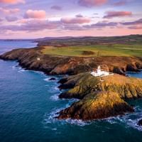 Witte vuurtoren op rotsachtige landtong in Pembrokeshire omringd door turquoise zee. Groene velden strekken zich landinwaarts uit.