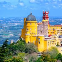 Kleurrijk Pena Paleis met gele en rode torens op een heuvel in Sintra, omringd door weelderig groen bos met uitzicht op dal.