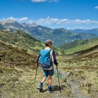 Vrouwelijke wandelaar met blauwe rugzak en wandelstokken op bergpad in Gschnitztal met Alpentoppen op de achtergrond.
