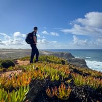 Wandelaar met rugzak op klif met kleurrijke vetplanten met uitzicht op de Atlantische Oceaan op de Rota Vicentina in Portugal.
