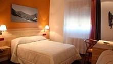 Moderne hotelkamer in Potes met wit bed, oranje accentmuur, berglandschap kunstwerk, bedlampjes en raam met natuurlijk licht.