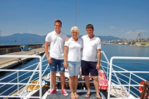 Drie bemanningsleden in witte uniformen staan op het dek van MS Kazimir met Kroatische kustbergen en haven op de achtergrond.