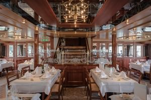 Elegante eetzaal op MS Switzerland met wit gedekte tafels, houten stoelen en een historisch schoepenrad als middelpunt onder een reflecterend plafond.