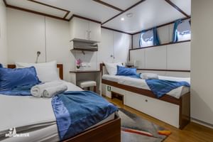 Tweepersoonshut op het benedendek van MY Olmissum met witte bedden, blauw beddengoed, ingebouwde kasten, kaptafel met spiegel en houten vloer.
