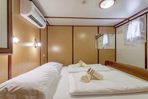 Moderne scheepshut op MS Amore bovendek met twee bedden, wit beddengoed, handdoeken, houtbetimmering, airconditioning en spiegel.
