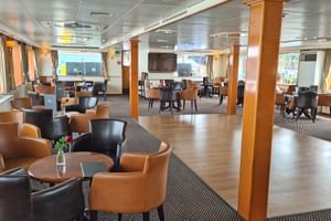 Moderne scheepsrestaurant salon met bruine leren stoelen, ronde tafels, houten pilaren en grote ramen. Het ruime interieur heeft eigentijdse inrichting.