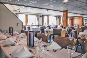 Interieur van MS De Willemstad restaurant met witte tafelkleden, wijnglazen en bruine stoelen. Grote ramen langs de wanden.