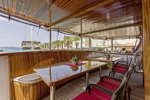 Interieur van MS Amore scheepssalon met houten plafond, eettafels, rode stoelen en grote ramen met uitzicht op een Middellandse Zeehaven.