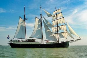 Driemast zeilschip Simmer Fan Fryslân met witte zeilen op kalm water onder blauwe hemel met wolken.