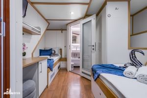 Compacte hut op benedendek van MY Olmissum met twee eenpersoonsbedden, blauw beddengoed, houten vloer en badkamer zichtbaar door deur.