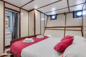 Lichte hut op het benedendek van MY Vita met twee bedden, wit beddengoed, roze lopers, patrijspoorten, houten afwerking en zichtbare badkamer.