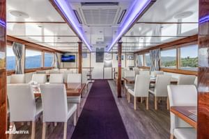 Interieur van MY Vita restaurant met witte stoelen, houten tafels, paarse plafondverlichting en grote ramen met uitzicht op de kust.