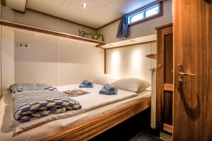 Gezellige dubbele cabine op MS Flora met opgemaakt bed, gestreepte deken, handdoeken, houten kast en raam met gordijn.