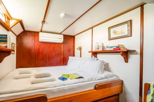 Compacte hut op MS Caprice met twee eenpersoonsbedden, wit beddengoed, houten lambrisering, airconditioning, plank met boeken en ingelijste kunst.
