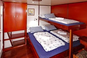Scheepshut met houten stapelbedden, nautisch beddengoed, rode wanden, kledingkast en ingelijste zeilkunst op MS Macek.