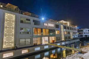 Wit cruiseschip H.S. Nebu met meerdere dekken afgemeerd aan de kade 's nachts met verlichte ramen en decoratieve verlichting, reflecterend in het water.