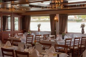 Interieur van MS Switzerland restaurant met gedekte tafels, witte tafelkleden, houten stoelen en grote ramen met uitzicht op het water.