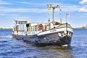 MS Flora, een wit en zwart passagiersschip met blauwe ramen, varend op kalm water onder een blauwe lucht met witte wolken.