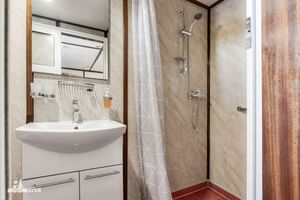 Compacte badkamer op MY Vita met witte wastafel, spiegel, douche met glazen deur, beige tegels en houten accenten.