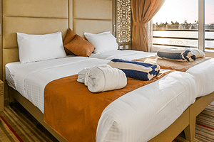 Moderne Nebu suite met twee bedden, wit beddengoed, oranje accenten en grote ramen met uitzicht op de Nijl in Egypte.