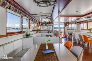 Lichte binnenkant van MY Olmissum salon met witte leren stoelen, houten tafels, oranje stoelen en grote ramen met panoramisch uitzicht op water.