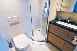 Moderne compacte badkamer op MS De Willemstad met glazen douche, wit toilet, houtlook wastafelmeubel met zwart blad.