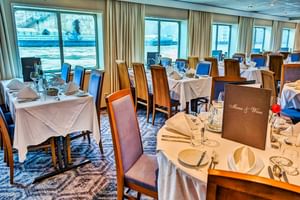 Elegant restaurant op SE Manon met tafels gedekt met wit linnen, wijnglazen en menukaarten. Grote ramen met uitzicht op het water.