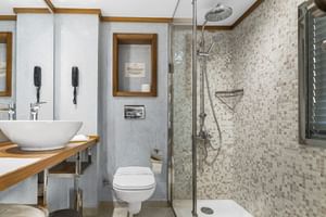 Moderne badkamer met mozaïek douche, glazen deur, witte opzetwastafel op houten blad, hangend toilet en houten accenten.